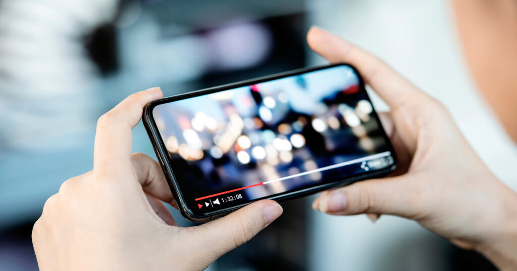 Cropped image of female hand holding smartphone and watching video while standing outdoor.