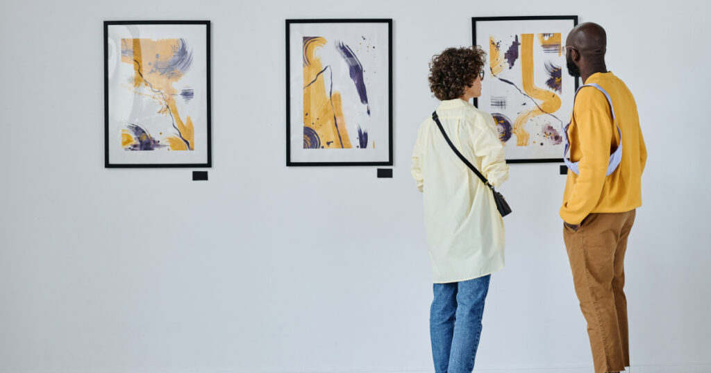 Rear view of young couple visiting art gallery, they standing and watching modern art