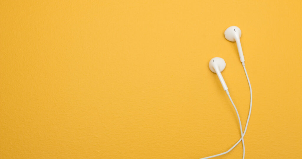 White earphones on yellow background, with copy space on the left.