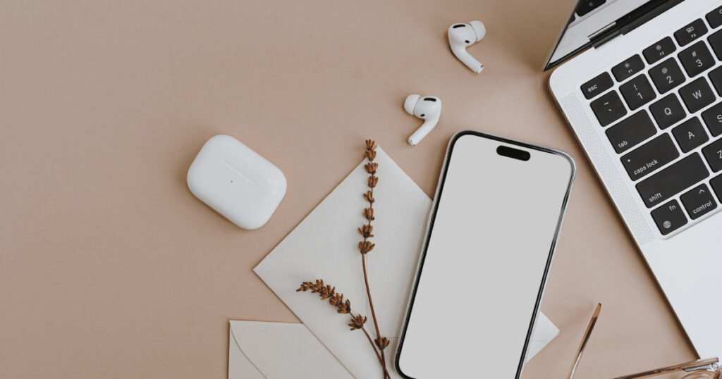 Office desk workspace desk. Cell phone with blank screen, laptop, earphones, dried grass on tan beige table. Styled flat lay mock up with empty copy space. Designed top view mobile phone mockup